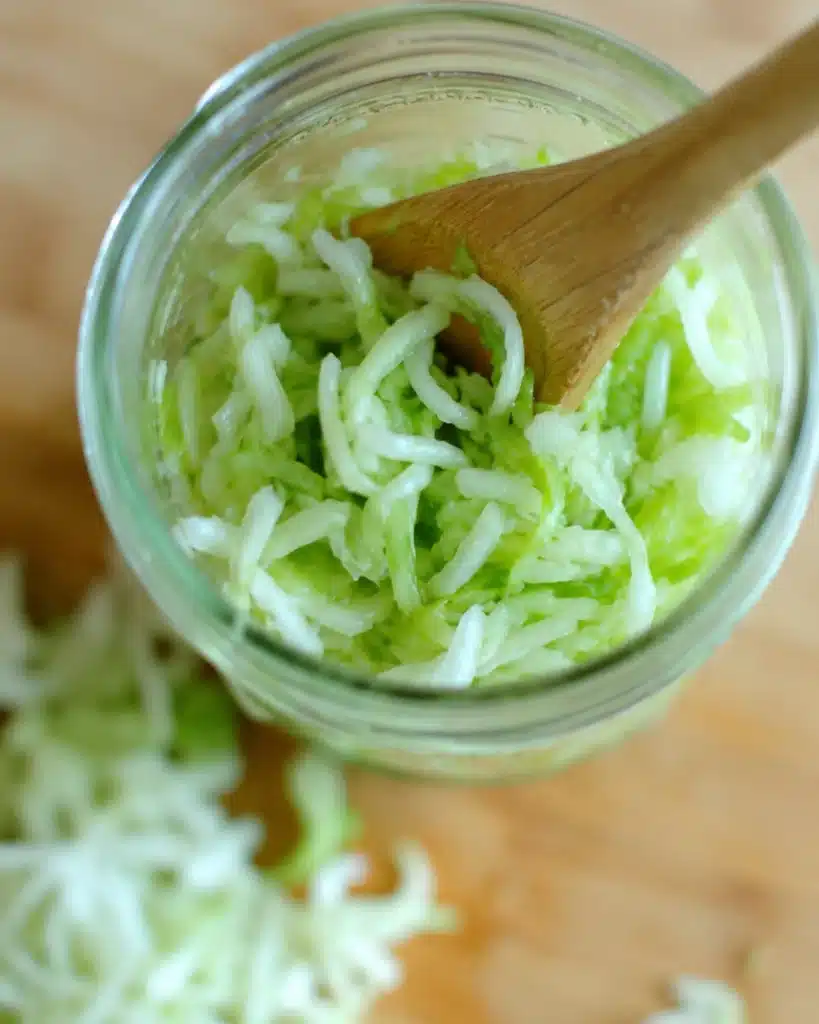 close up of shredded cabbage inside a jar being pressed with a wooden spoon