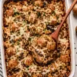 Overhead view of baked rice casserole with meatballs mushrooms and melted cheese being served