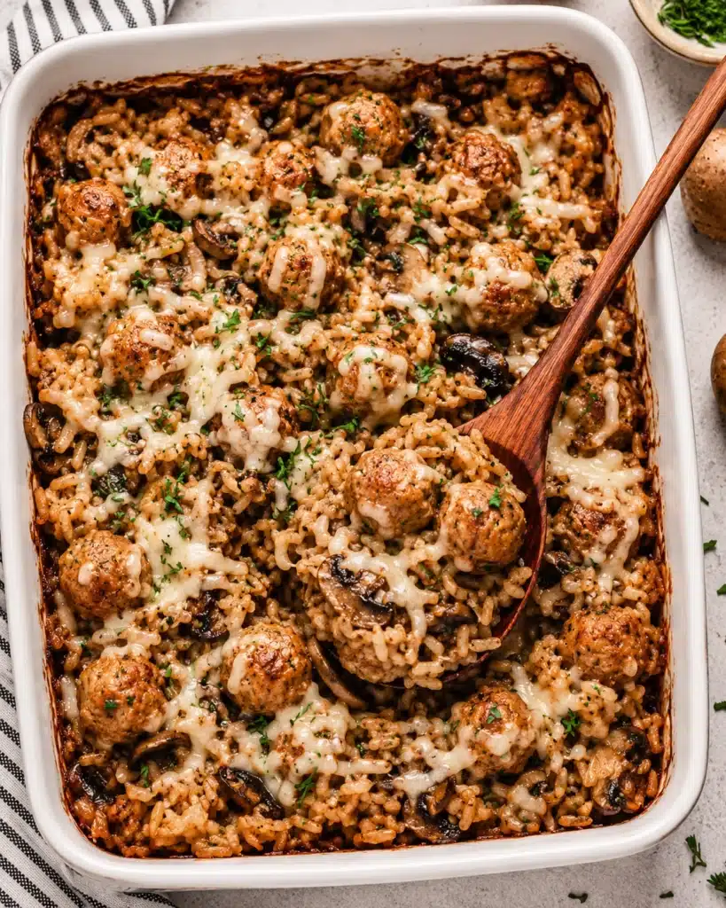 Overhead view of baked rice casserole with meatballs mushrooms and melted cheese being served