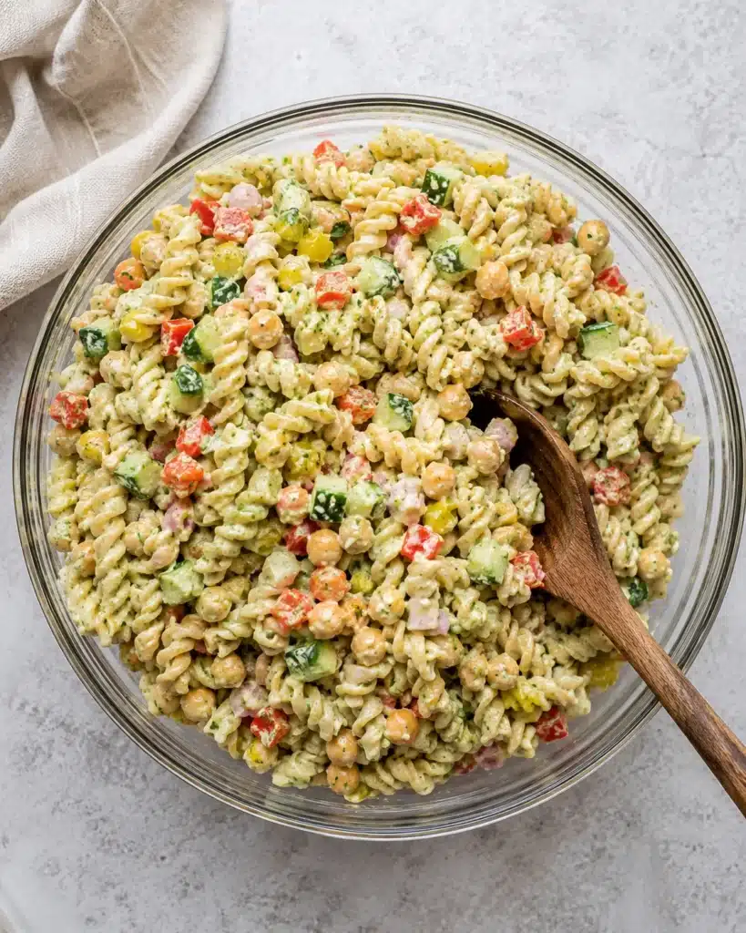 Creamy pasta salad with chickpeas, cucumber, and bell peppers in a glass bowl on a light surface