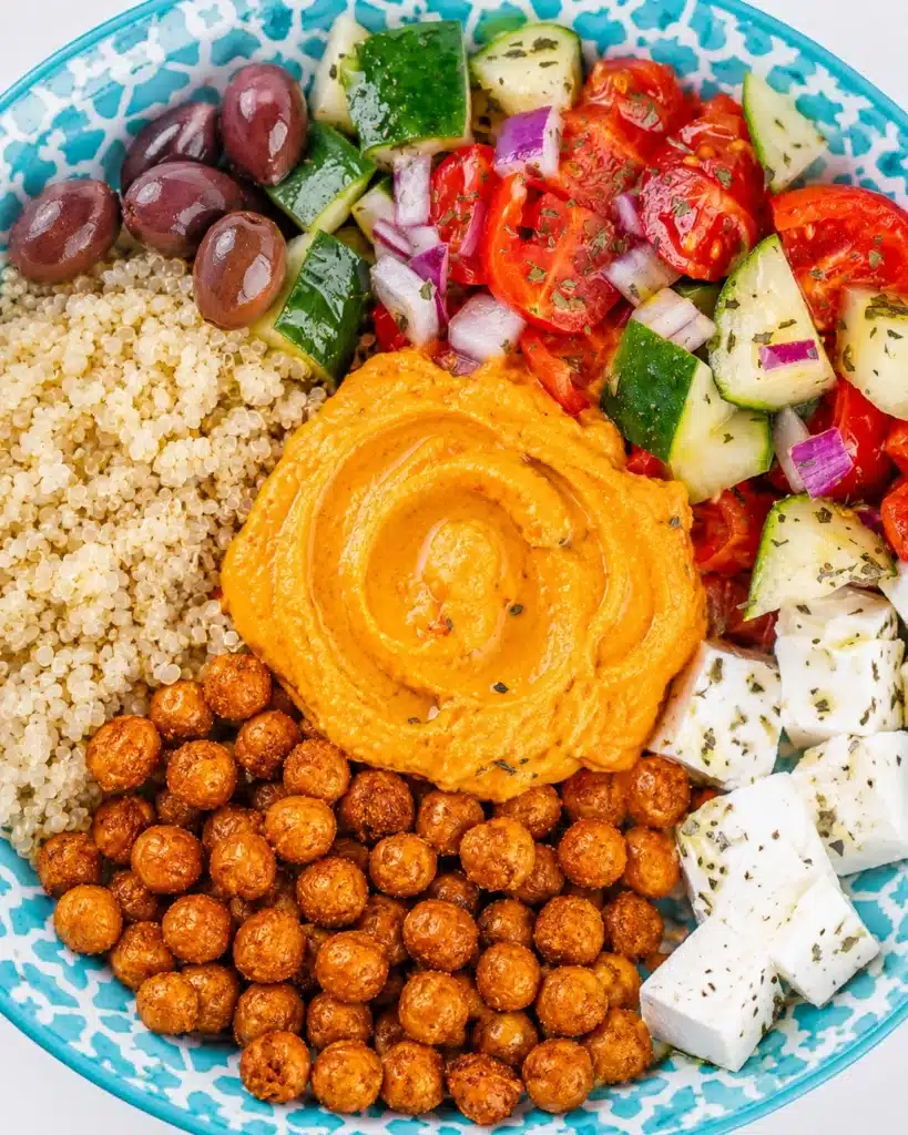 Colorful bowl with quinoa, roasted chickpeas, hummus, feta cheese, olives, and fresh chopped vegetables