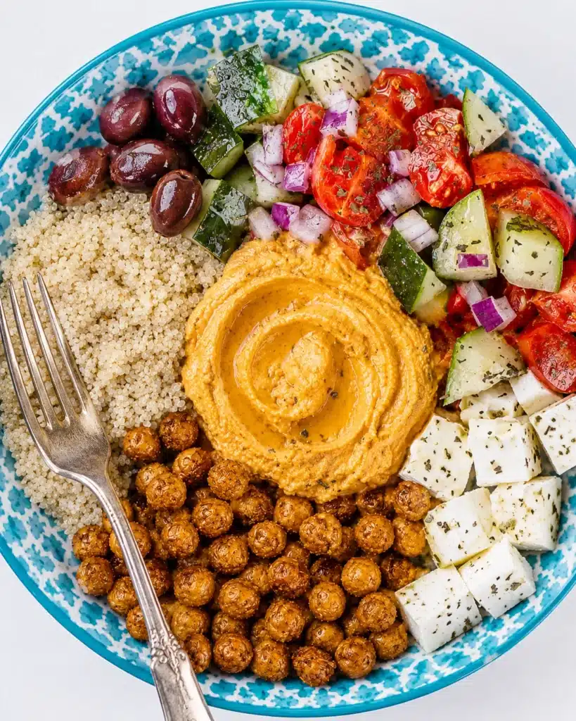 Top view bowl with quinoa, chickpeas, hummus, feta cubes, olives, and fresh salad with fork