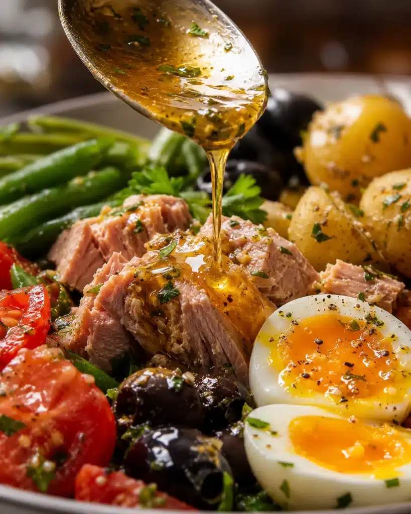 Olive oil dressing being poured over tuna, eggs, and vegetables