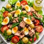 Fresh tuna salad with eggs, potatoes, green beans, and tomatoes on a white plate