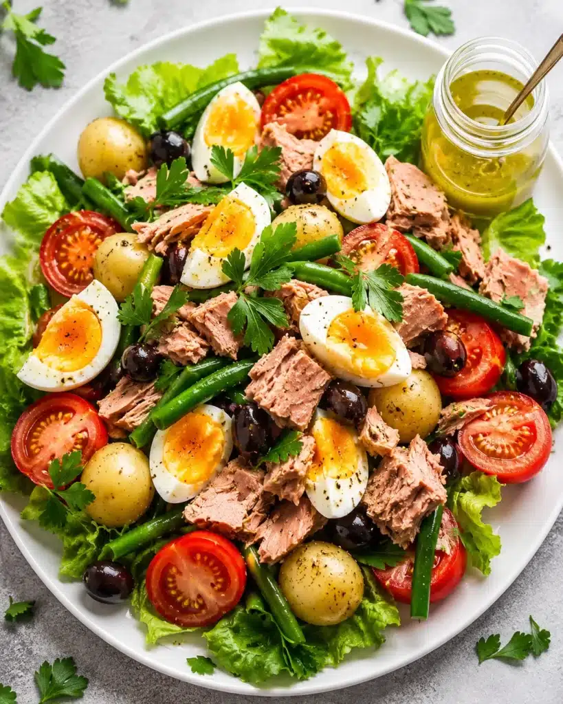Fresh tuna salad with eggs, potatoes, green beans, and tomatoes on a white plate