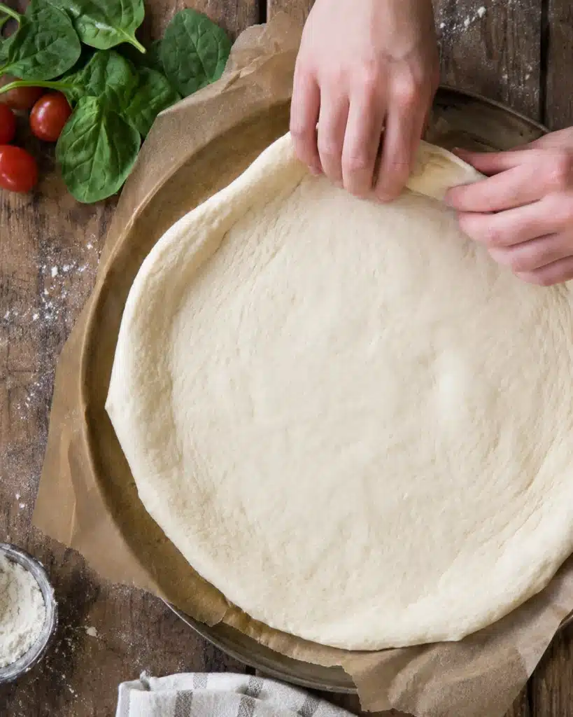 Hands stretching soft dough into a round shape on parchment paper