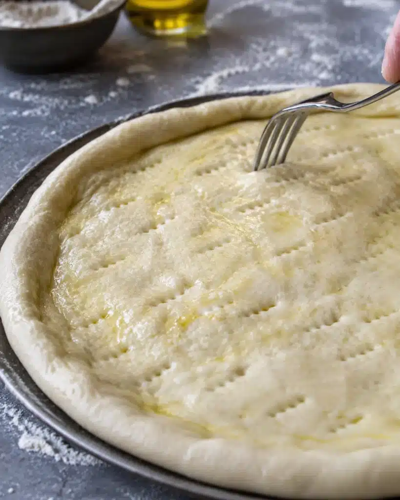 Raw dough shaped on a tray with fork holes and olive oil brushed on top