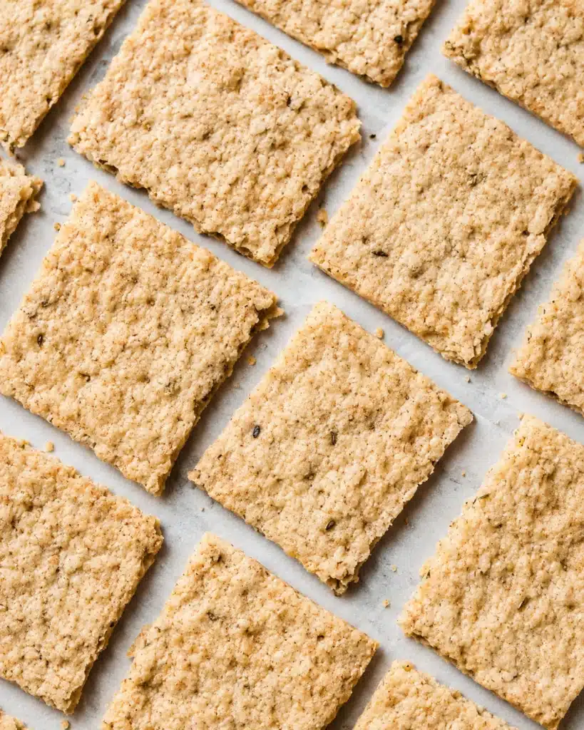 close up of golden square crackers with a textured surface on parchment paper
