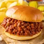Juicy sloppy joe sandwich filled with saucy ground beef on a soft toasted bun with chips and pickles on the side