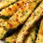 close up of zucchini sticks with melted cheese, black pepper and chopped herbs