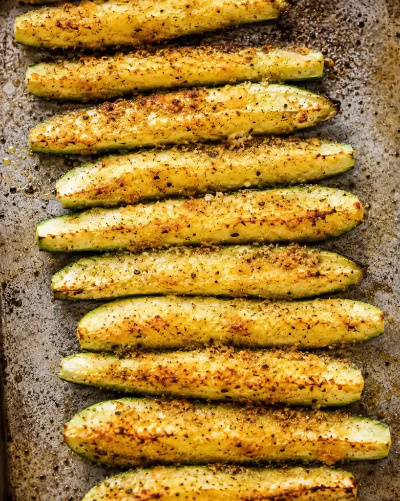 zucchini sticks arranged on a baking tray with seasoning and light browning