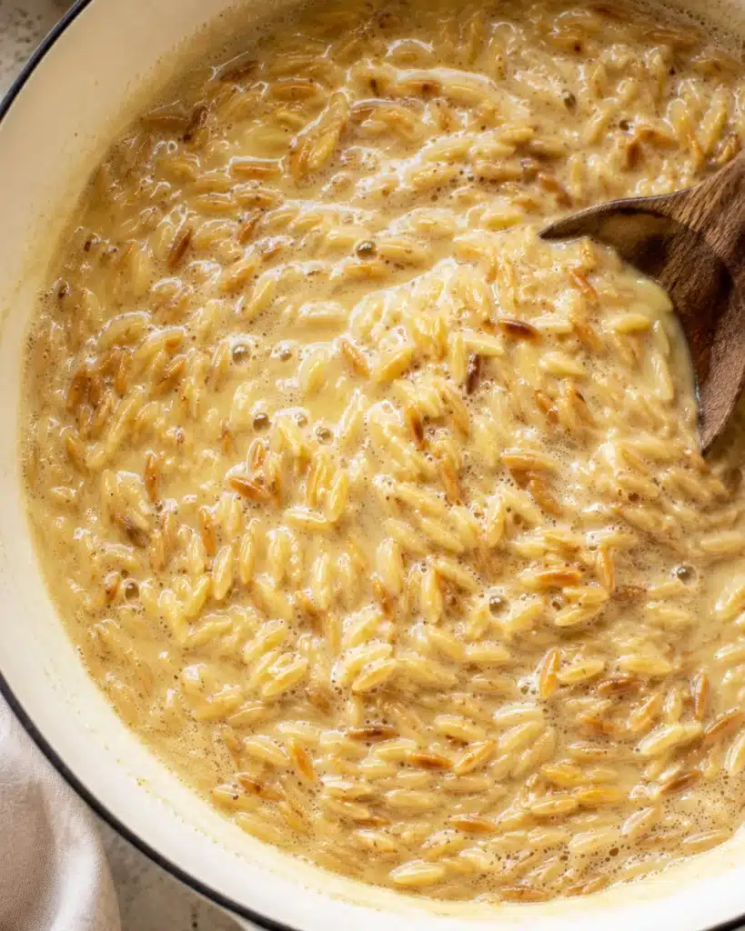 Orzo pasta simmering in a creamy garlic butter broth inside a skillet