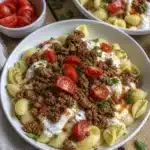 Close up of shell pasta topped with spiced ground beef, yogurt sauce, and fresh cherry tomatoes