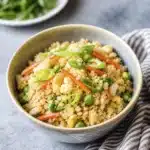 Bowl of cauliflower rice with peas carrots eggs and fresh green onion garnish