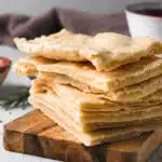 stack of freshly baked flatbread pieces on wooden board with soft folds and golden surface
