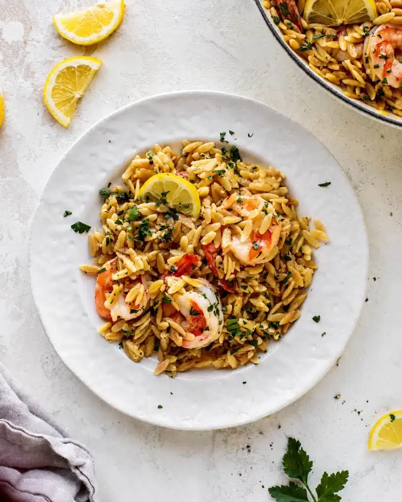 Plate of shrimp orzo garnished with parsley and a slice of lemon