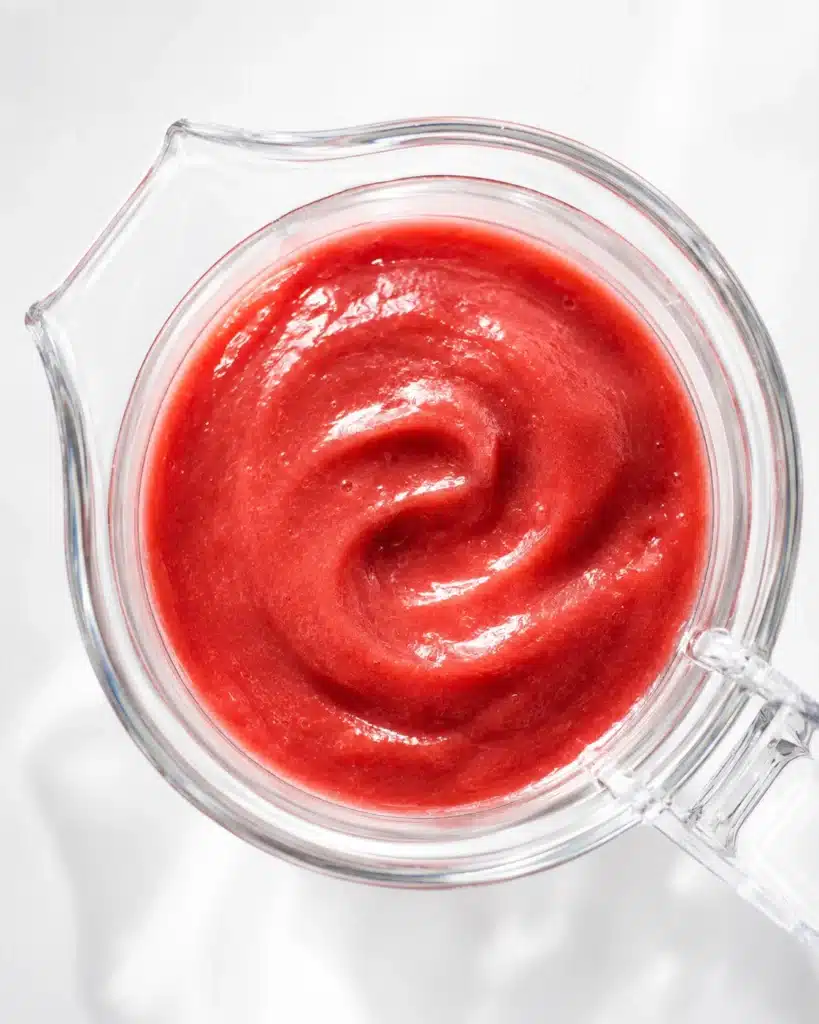 Top view of smooth pink rhubarb puree in a glass measuring cup on a bright white surface