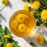 Top view of a glass cup filled with golden herbal tea and floating yellow flowers
