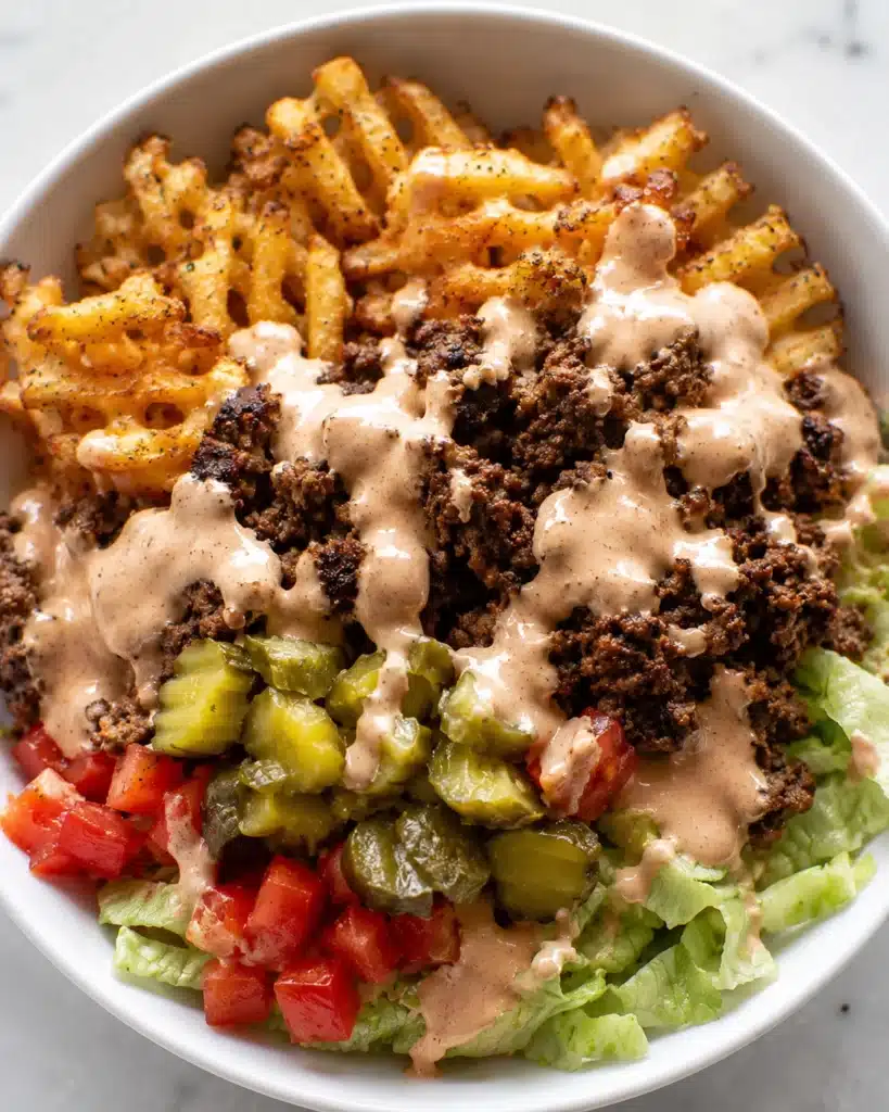 Close up of crispy waffle fries with seasoned beef, chopped vegetables, and creamy dressing