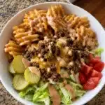 Cheesy beef bowl with waffle fries, pickles, tomatoes, lettuce, and creamy sauce