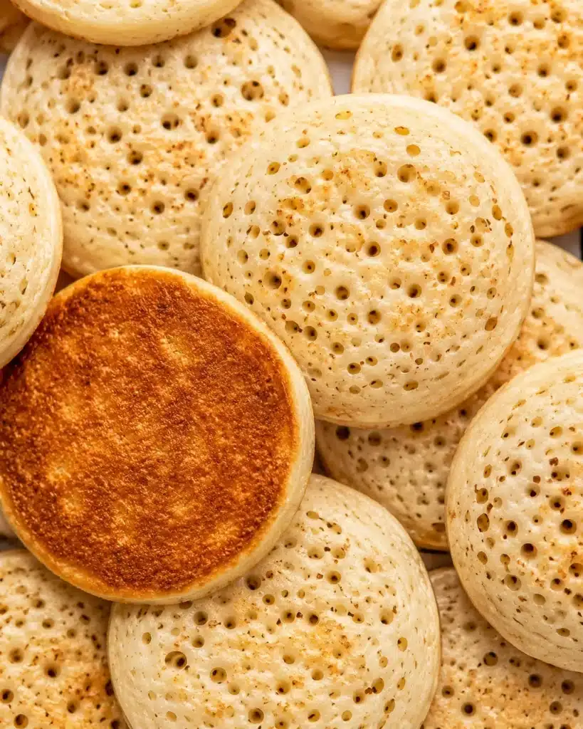 top view of several crumpets showing detailed holes and one toasted golden bottom