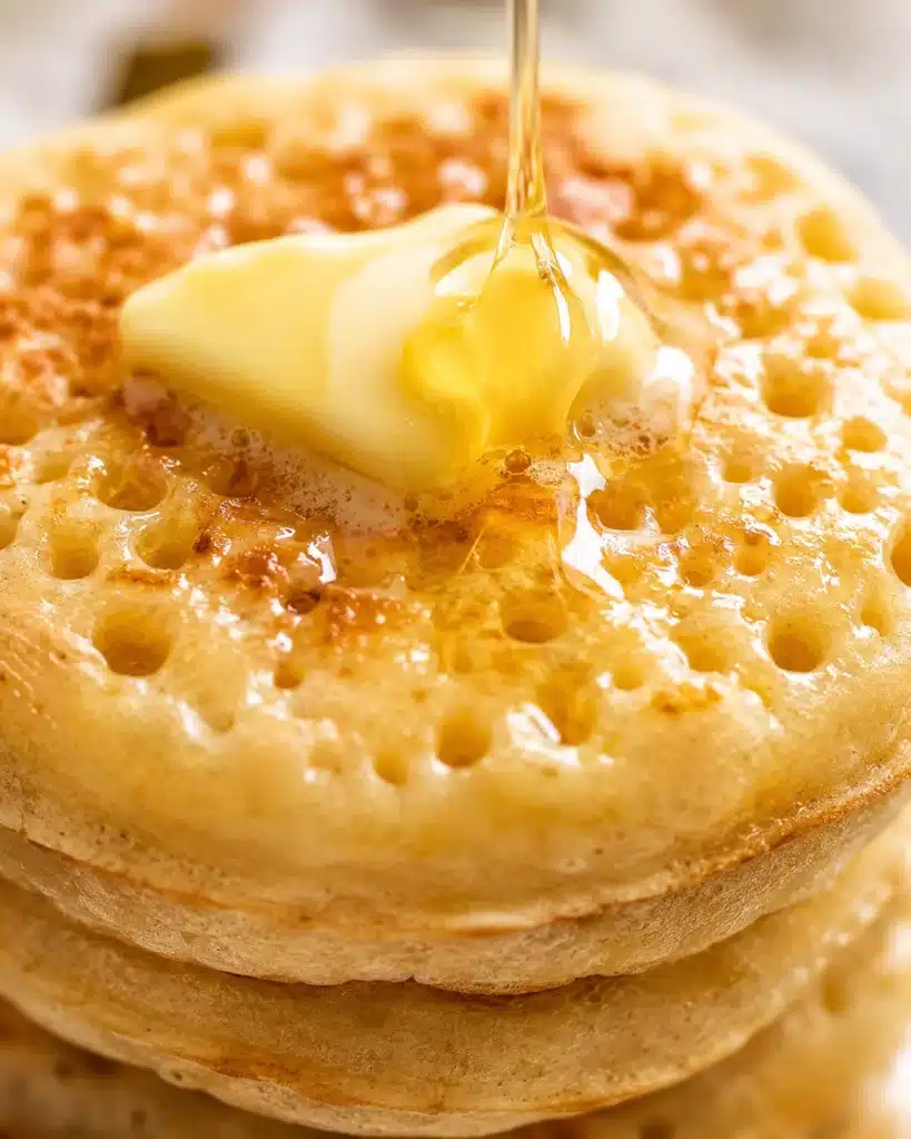 honey being poured over butter on a crumpet showing glossy texture and soft interior