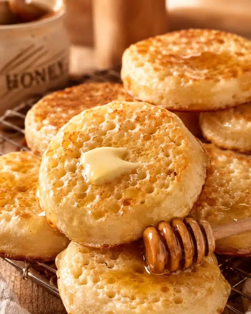 stack of warm crumpets with butter and honey drizzle on top on a rustic surface