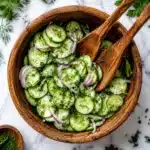 Cucumber slices with red onion and herbs served in a wooden bowl with salad spoons