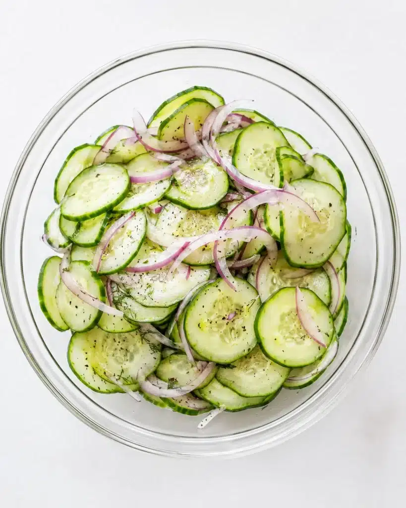 Clear bowl filled with sliced cucumbers and onions lightly seasoned on a white background