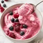 Close up of a spoon lifting creamy berry yogurt dessert from a bowl with fresh berries