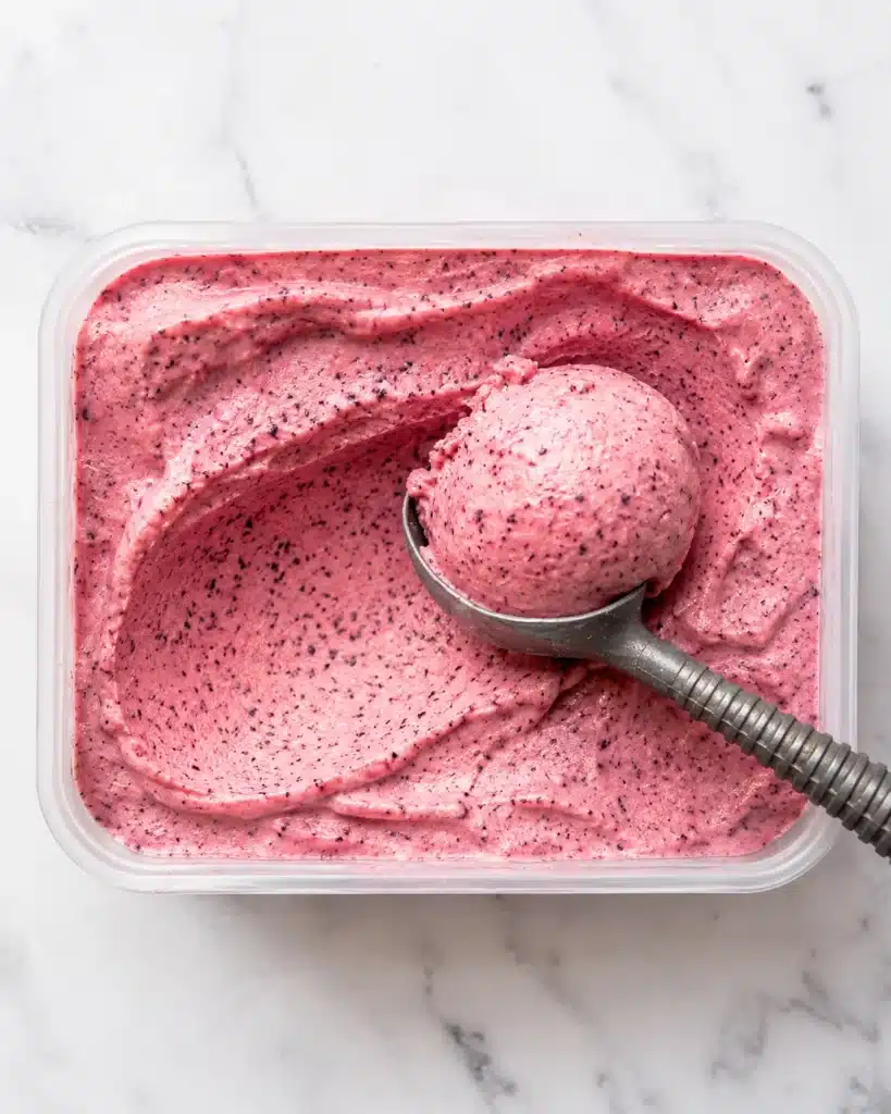Homemade berry yogurt dessert in a container with a smooth scoop taken out