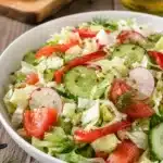 Close up of a fork lifting a bite of salad with cucumber, radish, lettuce, and herbs