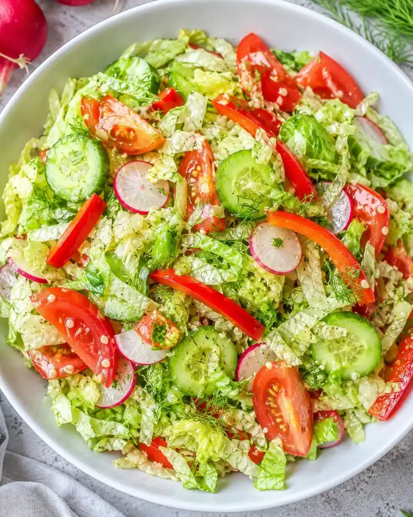 Fresh vegetable salad with cucumber slices, radishes, tomatoes, and herbs in a white bowl