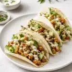 Three soft tacos filled with chickpeas, cucumber, herbs, and creamy dressing on a white plate