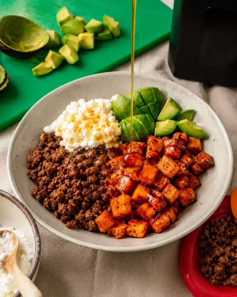 bowl with roasted sweet potatoes ground beef cottage cheese avocado and honey drizzle