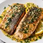 Golden seared trout with herbs and lemon on a white plate