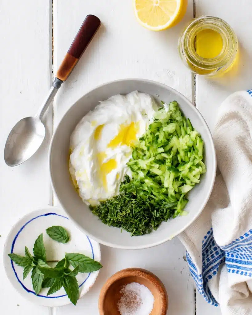Greek yogurt with grated cucumber and herbs in a bowl ready to be mixed
