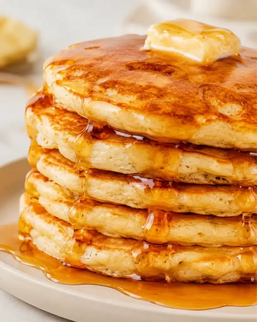 Stack of golden brown fluffy pancakes with melting butter and maple syrup