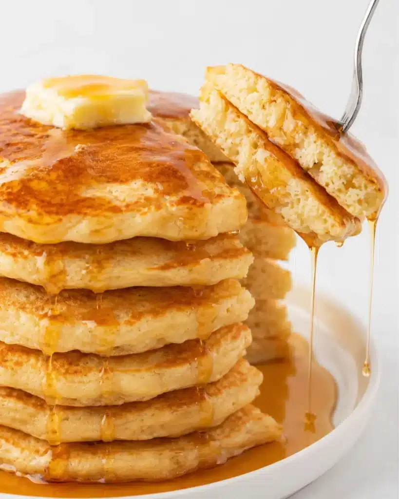 Thick fluffy pancakes cooking on a black nonstick griddle with bubbles on the surface