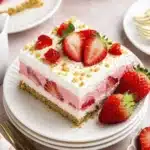 Layered dessert square with whipped topping and sliced strawberries on a white plate
